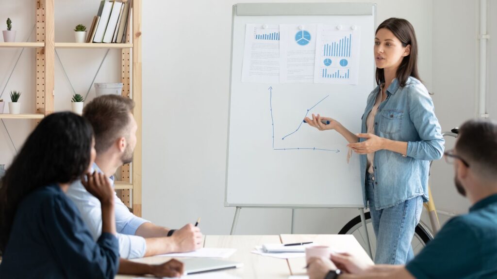 a woman in a meeting with other co-workers discussing charts and graphs, representing market research.
