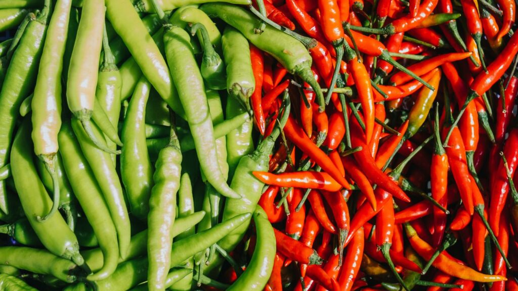 A close up of a harvest of green and red chili peppers