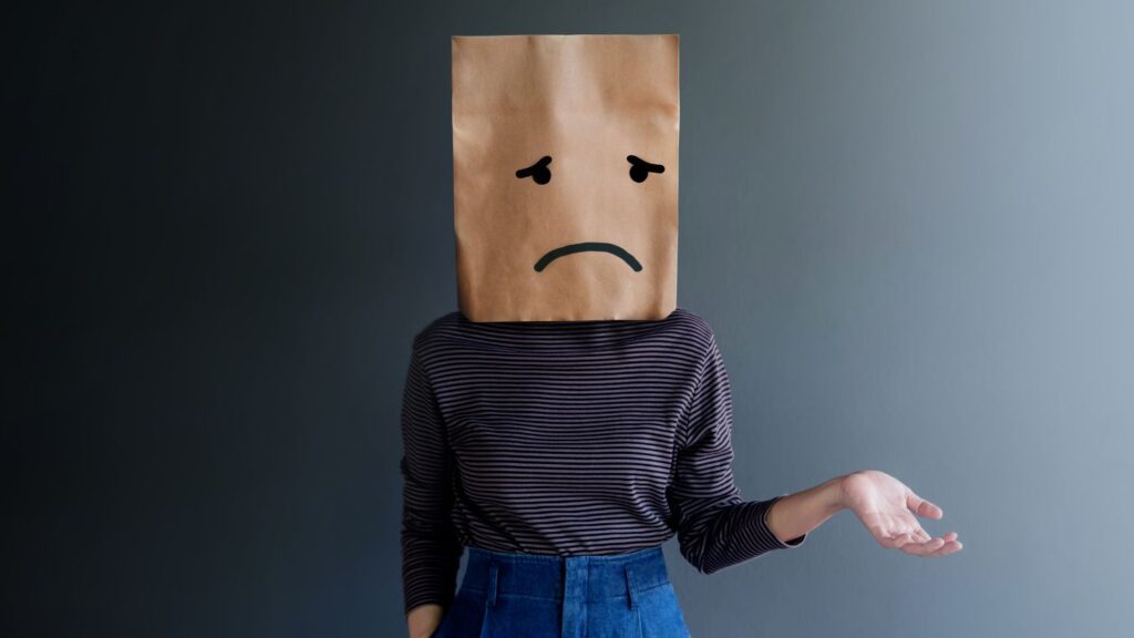 Woman with her head covered with a paper bag with a sad face drawn on it