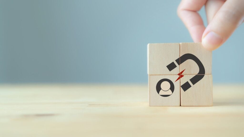 Lead generation, customer retention concept. Inbound marketing strategy. Hand puts wooden cubes with magnet attracts customer icons on beautiful grey background and copy space. Brand loyalty banner.