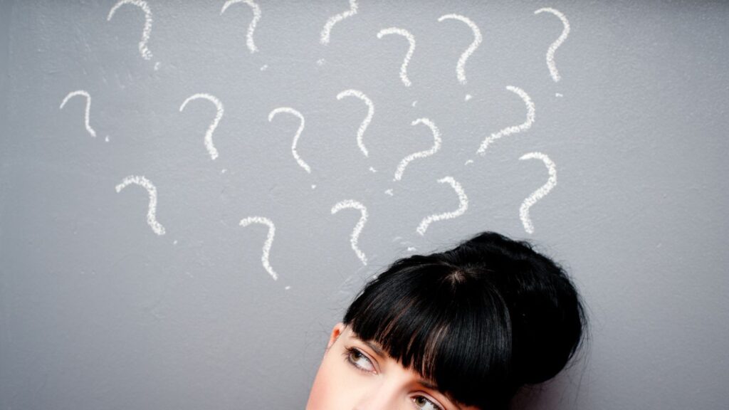 A lady looking at question marks written on a blackboard.